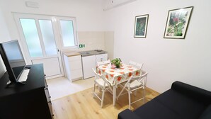 Et kompakt værelse med tekøkken, et spisebord med stole, en sort sofa og to billeder hængende på væggen.