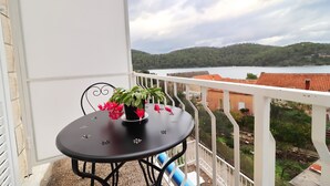 En balkon med et rundt bord og plantekasser, med udsigt over vand og bakker.