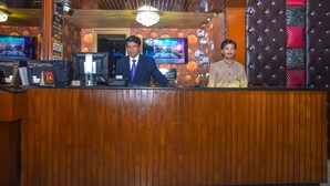 A reception desk with two staff members, a television screen, and a chandelier. - Hotel Faran (Karachi)