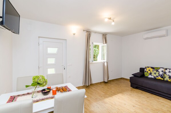 A room with a dining table, a sofa, a TV, and a window with curtains.
