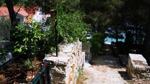 Un sendero de piedra que atraviesa un jardín con un muro de piedra a un lado y un edificio de techo rojo al fondo.