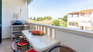 Een balkon met een ontbijttafel, inclusief stukken watermeloen en sinaasappelsap, met uitzicht op een woonwijk.