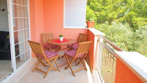 Ein Balkon mit Tisch und Stühlen, einem Blumentopf und einem Fenster mit Blick ins Grüne.