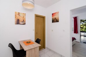 A small, bright room with a wooden door, a dining table with chairs, and two wall-mounted pictures.