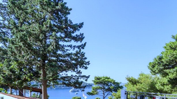 A terrace with a table and chairs, a wooden lounge chair, and a view of the sea.
