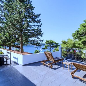 A terrace with a table and chairs, a wooden lounge chair, and a view of the sea.