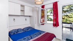 A bedroom with a bed, white wardrobe, and a window with red curtains.