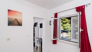 A room with a view of a dock and sunset, a window with red curtains, a white chair, and a desk with a computer.