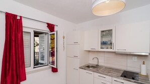 A compact kitchen with white cabinets, a sink, and a window with red curtains.