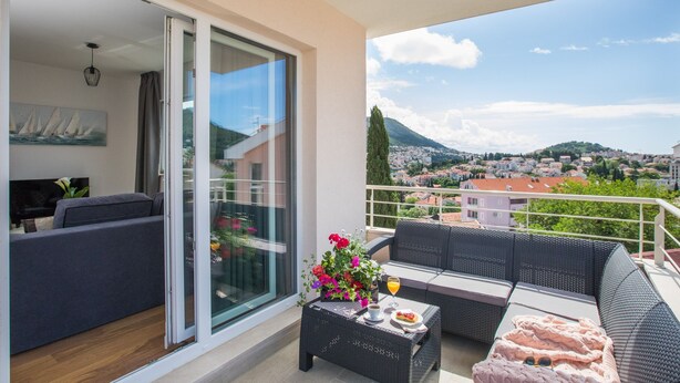 A balcony with a sofa, a table with a drink and food, and a city view.