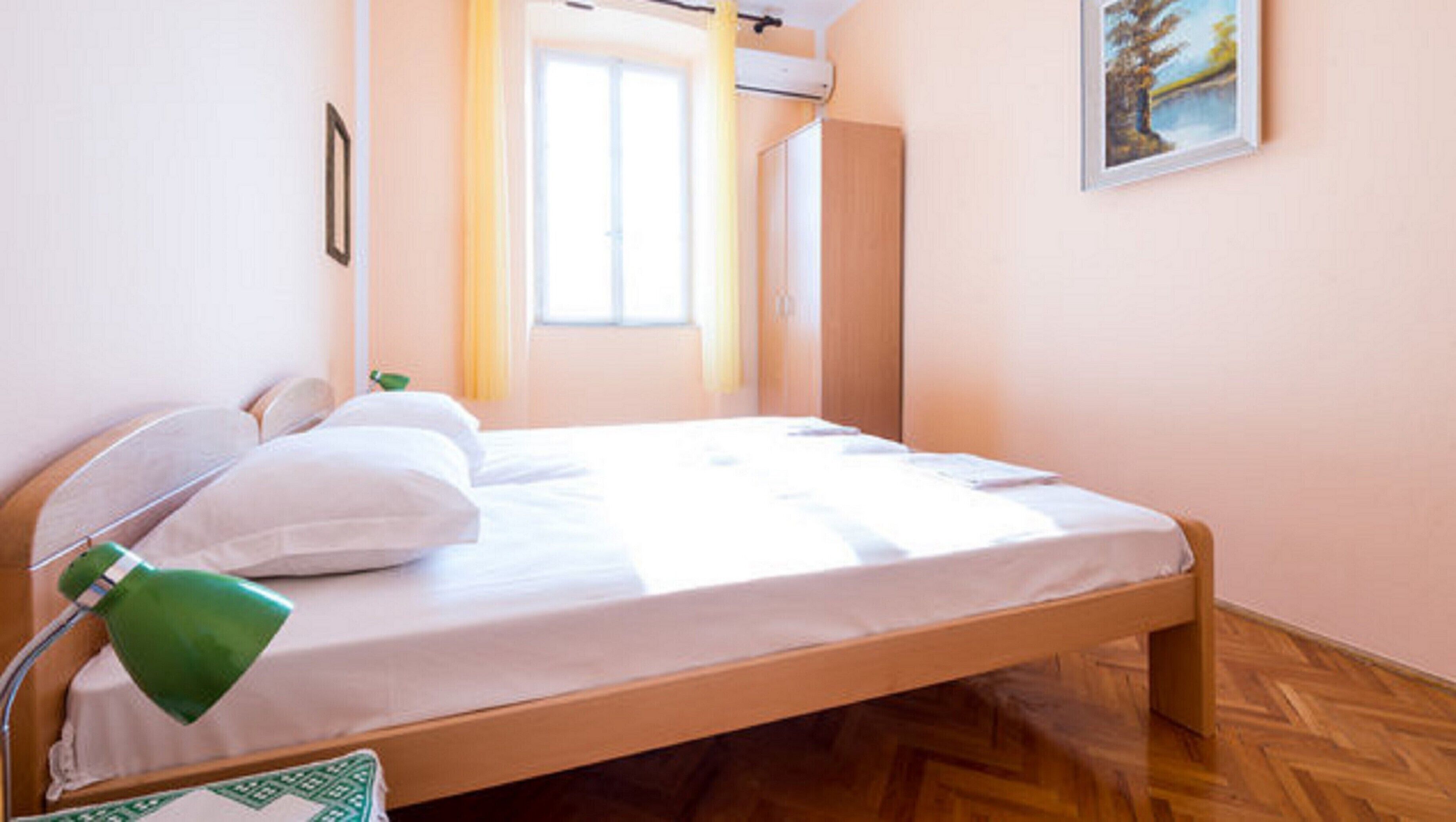A neatly made bed with white linens, a green bedside lamp, and a framed picture on the wall.