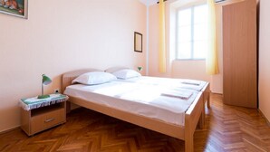 Un dormitorio con una cama de madera, una mesita de noche, un armario pequeño, una ventana con cortinas y una puerta.