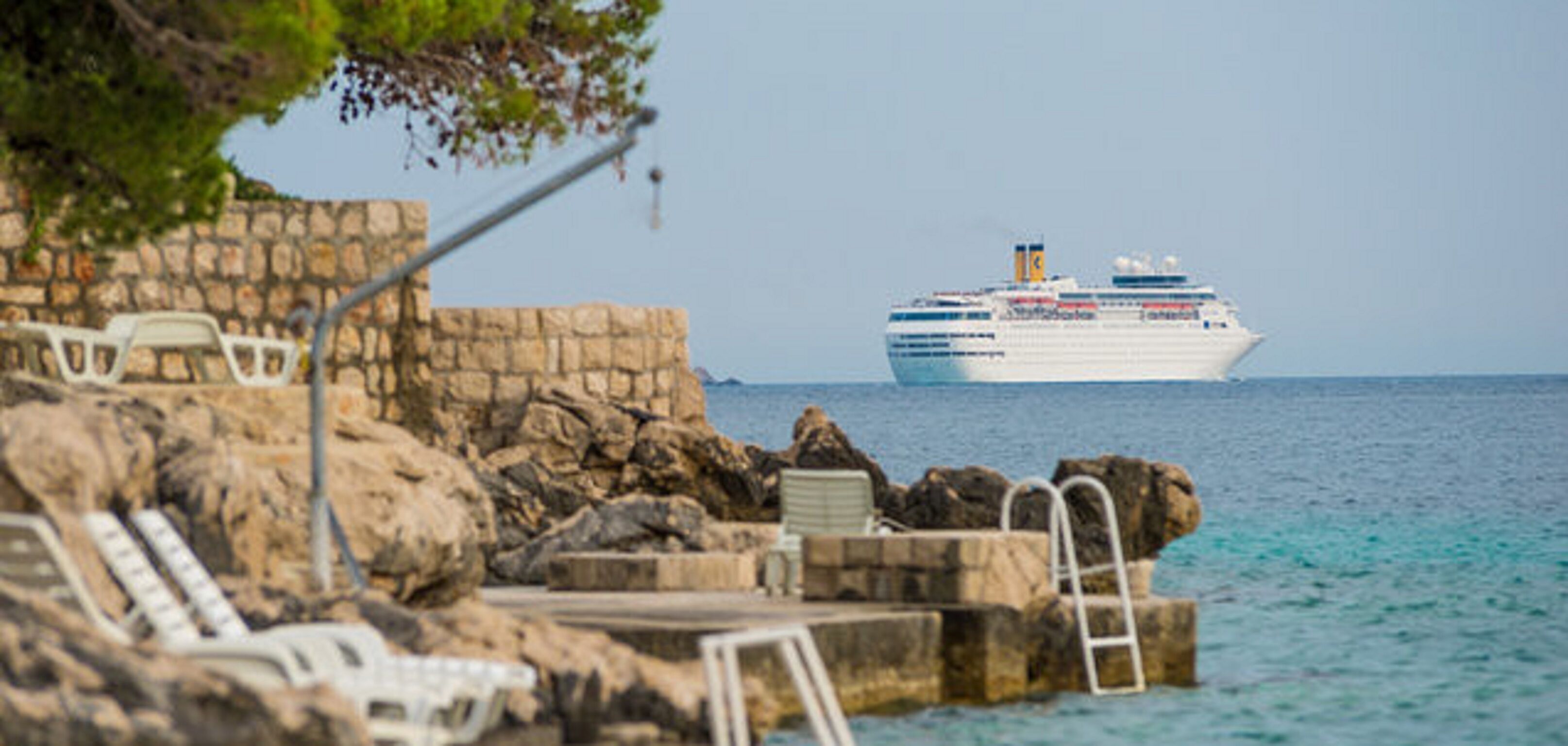 A cruise ship docked at a rocky pier with a pool area and lounge chairs.
