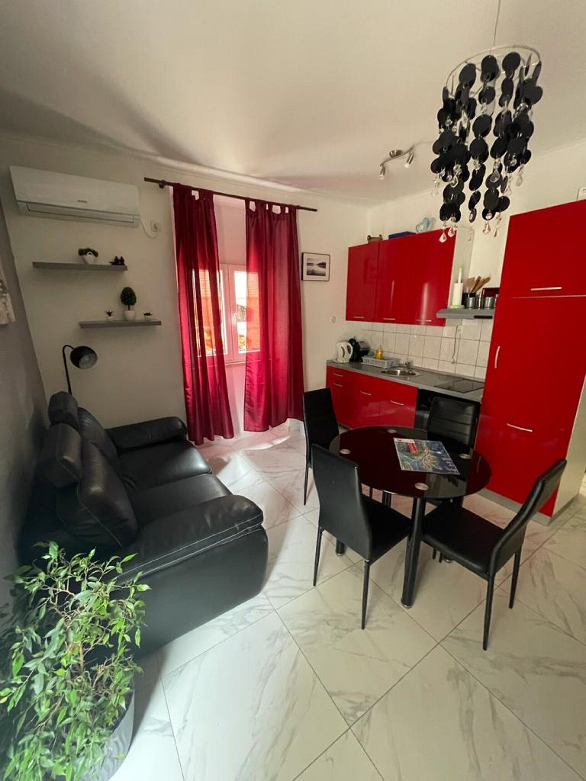 En kompakt opholdsstue med spiseplads, sofa, et lille køkken med røde skabe og en loftlampe.