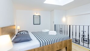 Un dormitorio moderno con una cama de madera, ropa de cama a rayas, un tragaluz y una barandilla de metal negro.