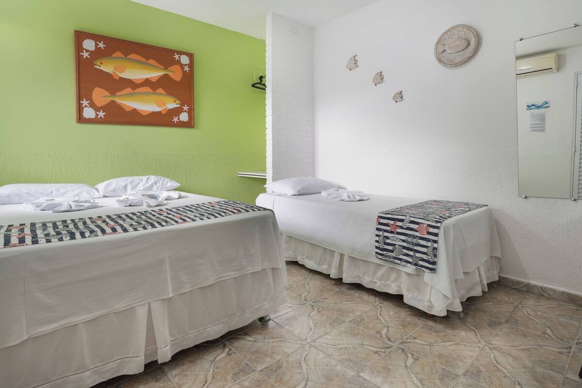 Ein Hotelzimmer mit zwei Betten, einer grünen Wand, einem Fischgemälde und einem kleinen Tisch mit kariertem Tischlauf.