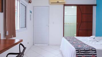 A hotel room with a bed, a desk, a chair, a wardrobe, and a bathroom with a glass door.