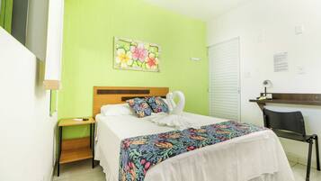 Habitación de hotel con cama, escritorio, silla, mesita de noche y pared verde con una pintura floral.