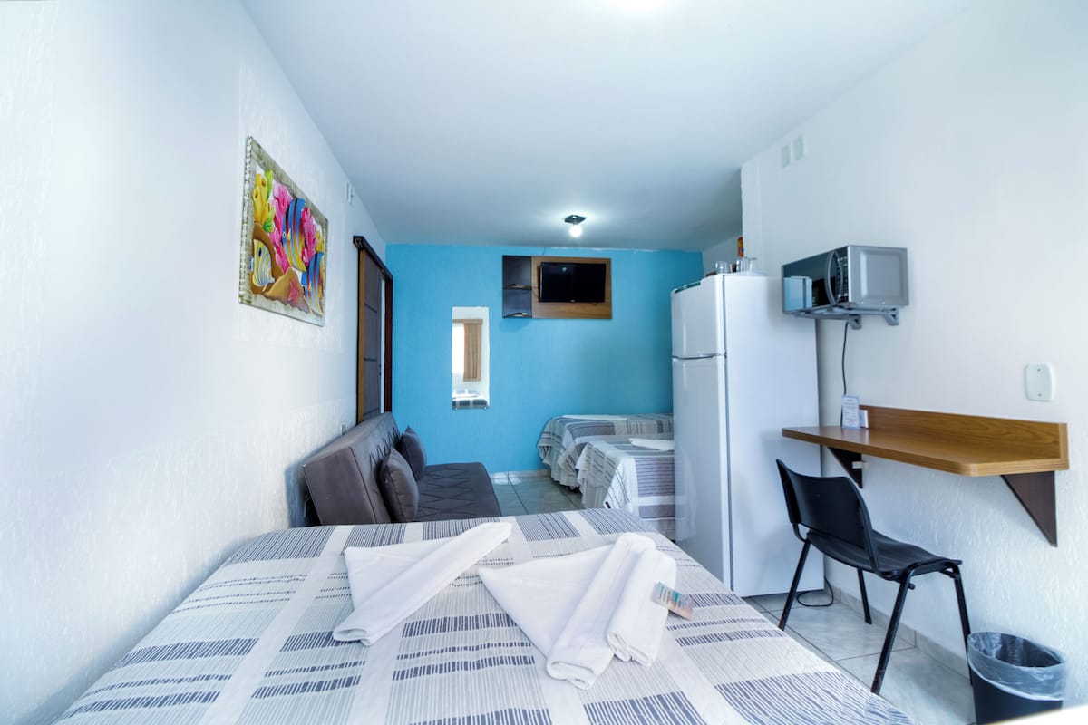 Ein kleines Hotelzimmer mit einem Bett, einem Schreibtisch, einem Stuhl, einem Kühlschrank und einem Fernseher.