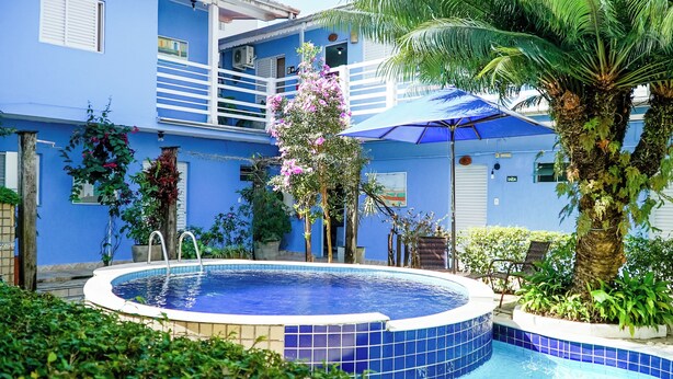 Ein blaues Gebäude mit Schwimmbad, umgeben von viel Grün und einer Palme.