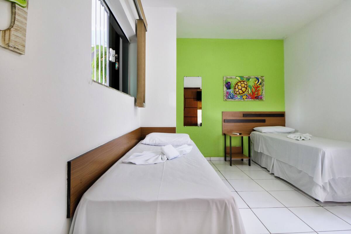 Ein Hotelzimmer mit zwei Einzelbetten, einem Holzkopfteil, einer grünen Akzentwand und einem farbenfrohen Gemälde.