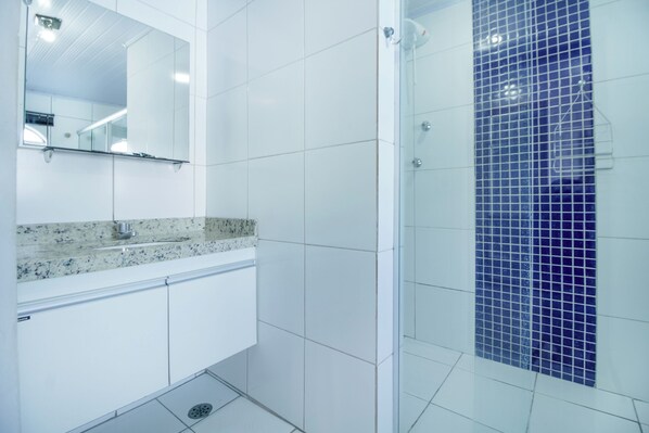 Un baño con azulejos blancos, encimera de granito, espejo y ducha con mosaicos azules.