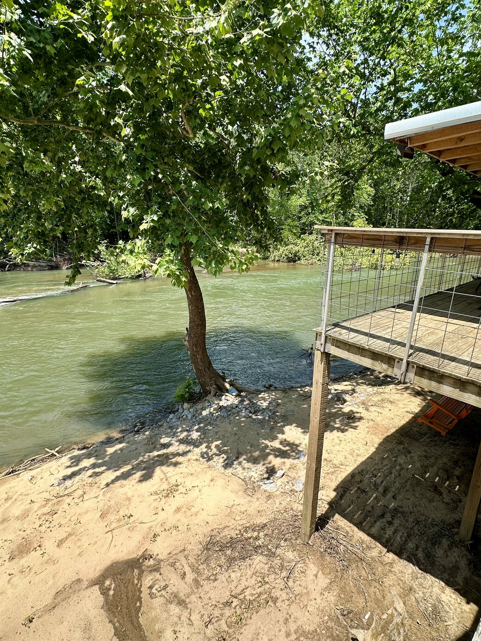 Une vue sur la rivière, avec une terrasse en bois et une rambarde en métal surplombant l’eau.