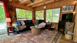Een gezellig houten blokhut interieur met een bank, een ronde salontafel, een open haard en grote ramen.