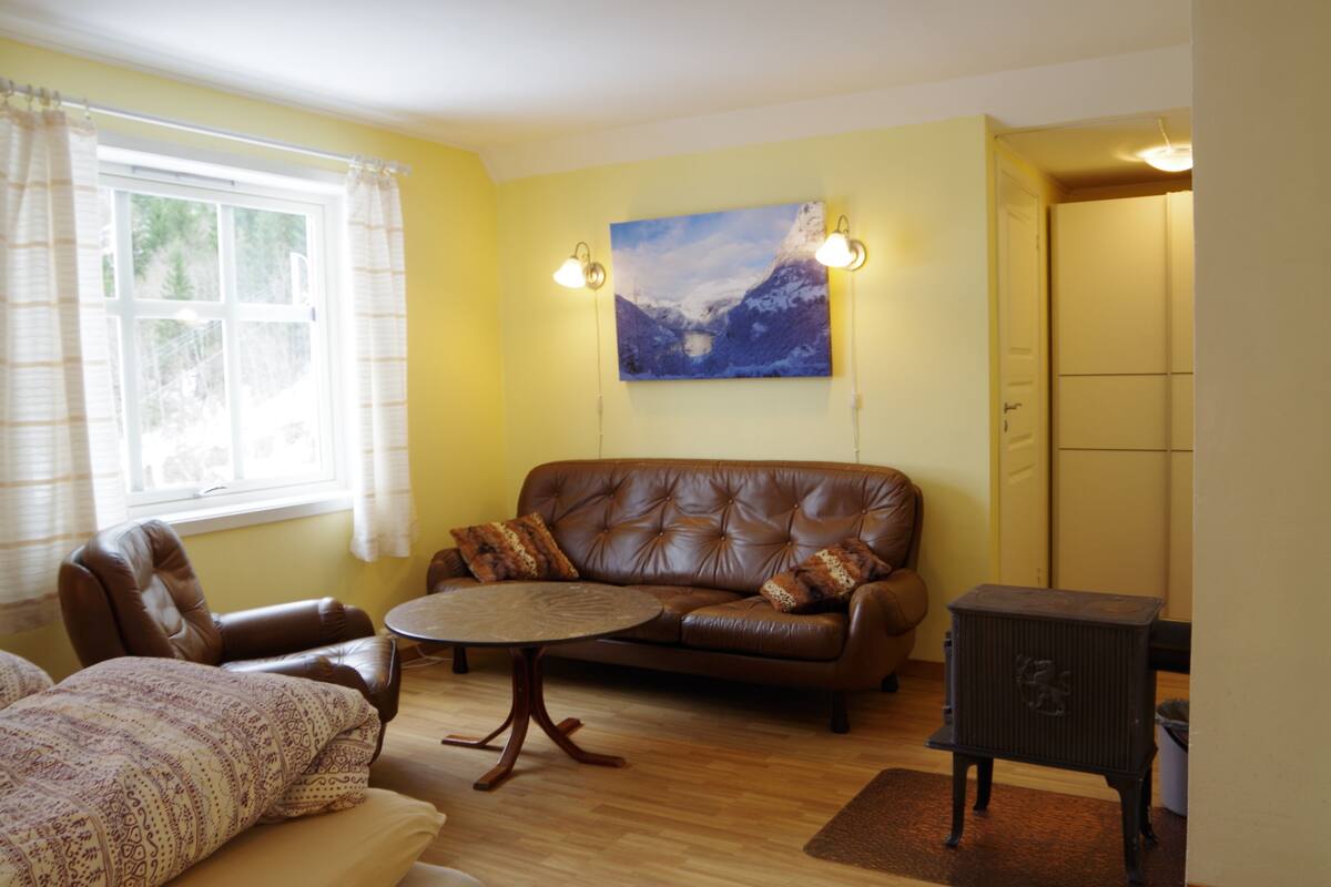 A living room with a brown leather sofa, a round coffee table, and a painting of a mountain on the wall.