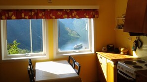 A kitchen with a view of a mountainous landscape through two windows, a table with chairs, and a stove. - Lunheim Accomodation (Stranda)