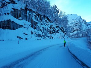 A snow-covered road with a person in a bright jacket standing by the roadside. - Lunheim Accomodation (Stranda)