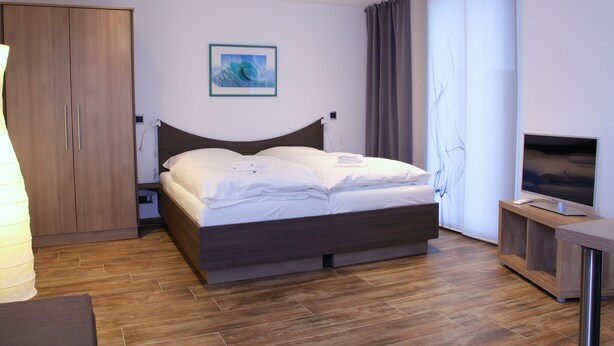A modern hotel room with a wooden bed, a flat-screen TV, and a large window with curtains.