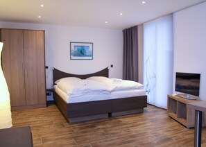 A modern hotel room with a wooden bed, a flat-screen TV, and a large window with curtains. - Apartments Peters (Burscheid)