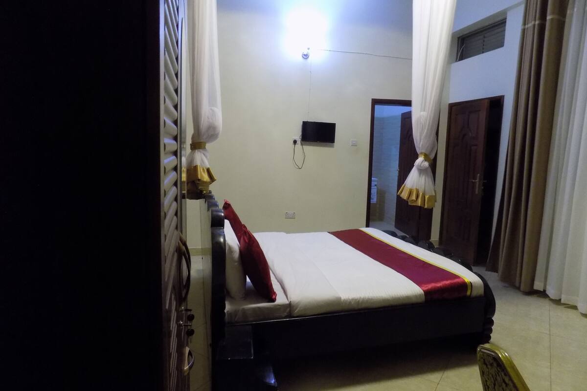 Una habitación de hotel con cama, cortinas, televisor y puerta.