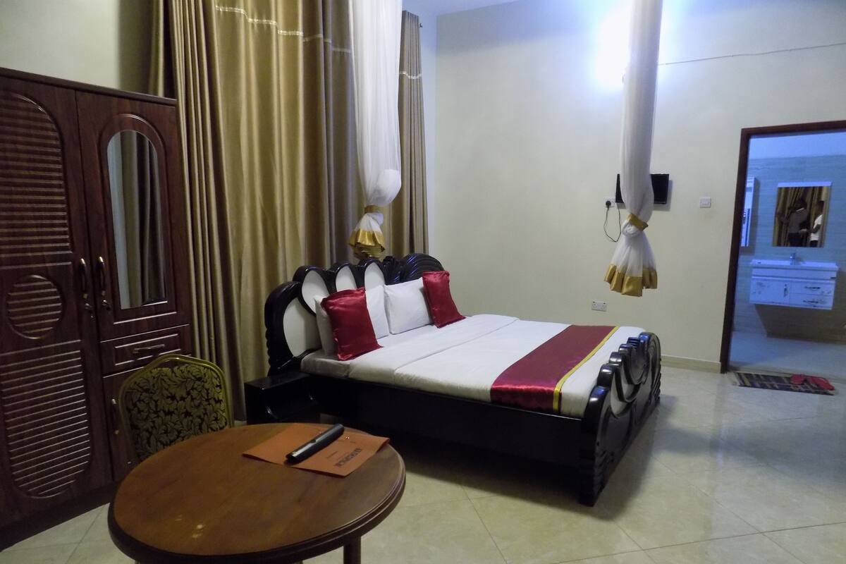 Una habitación de hotel con una cama, una silla de madera, una mesa redonda y un armario.