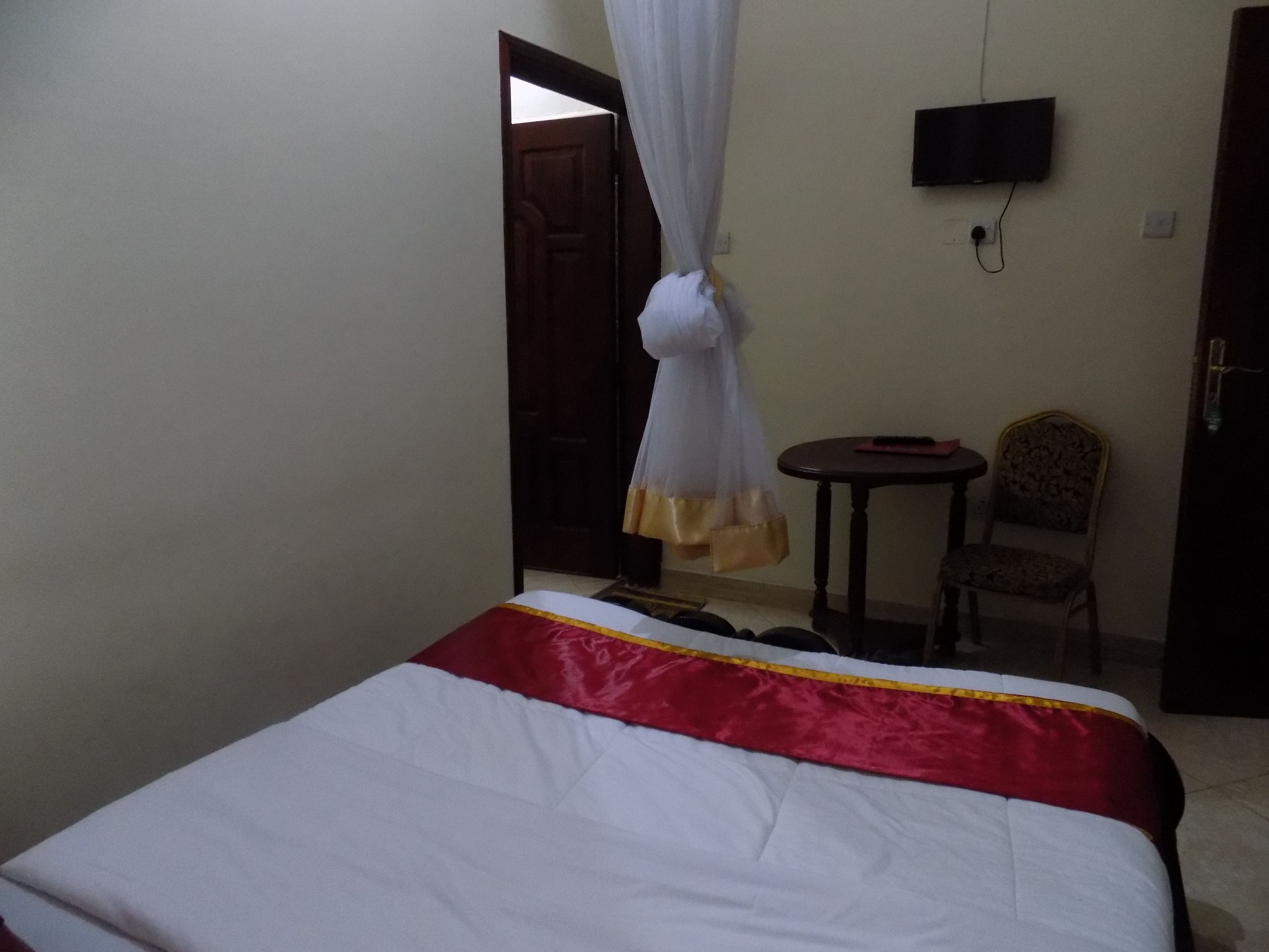 A bedroom with a bed, a TV mounted on the wall, a chair, and a small table.