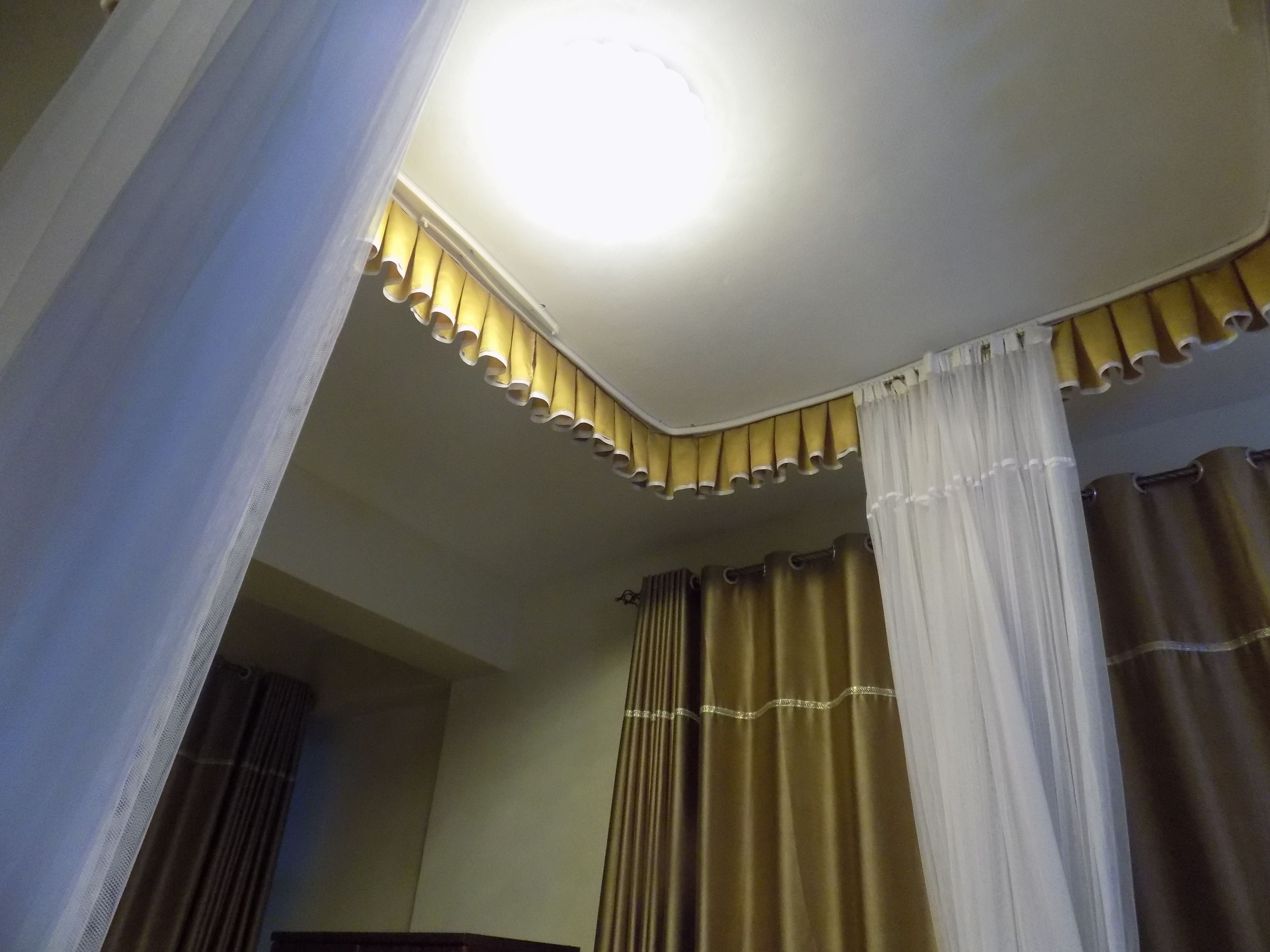 Una habitación con una lámpara en el techo, una esquina con detalles decorativos y cortinas.