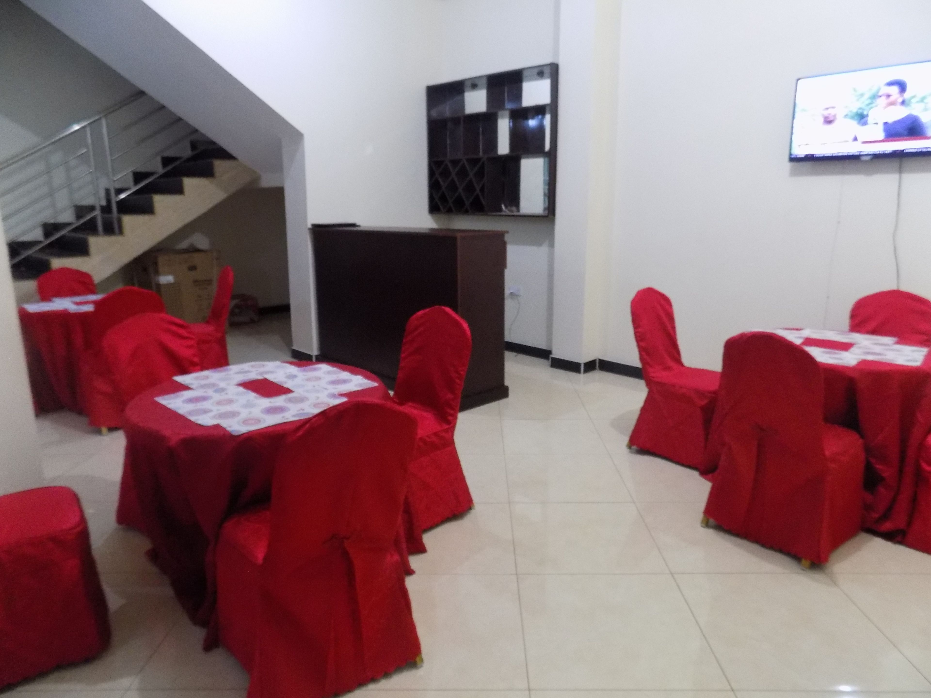 A conference room with red-covered tables and chairs, a staircase in the background, and a TV mounted on the wall.