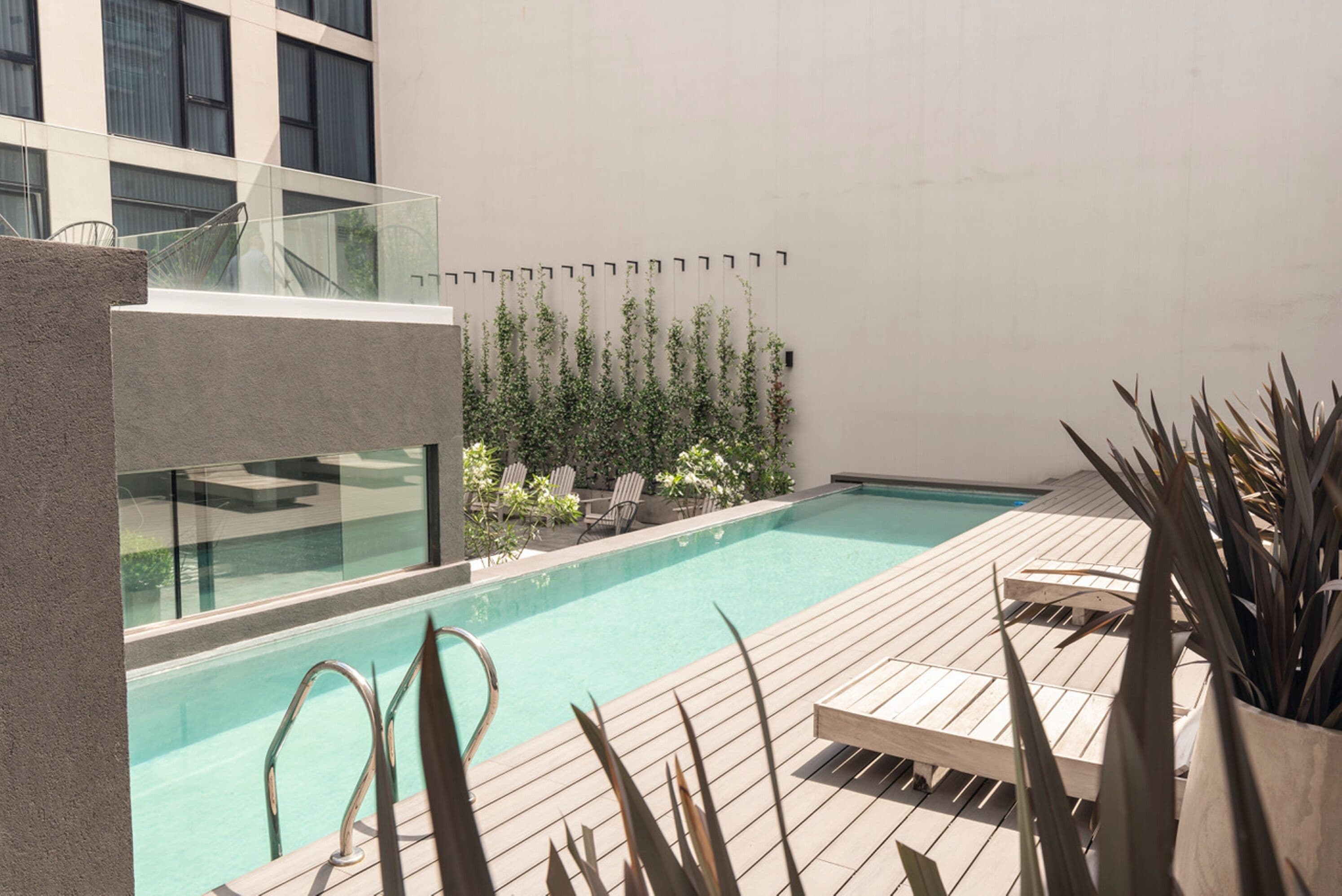 A modern outdoor pool area with a wooden deck, lounge chairs, and a glass balustrade.