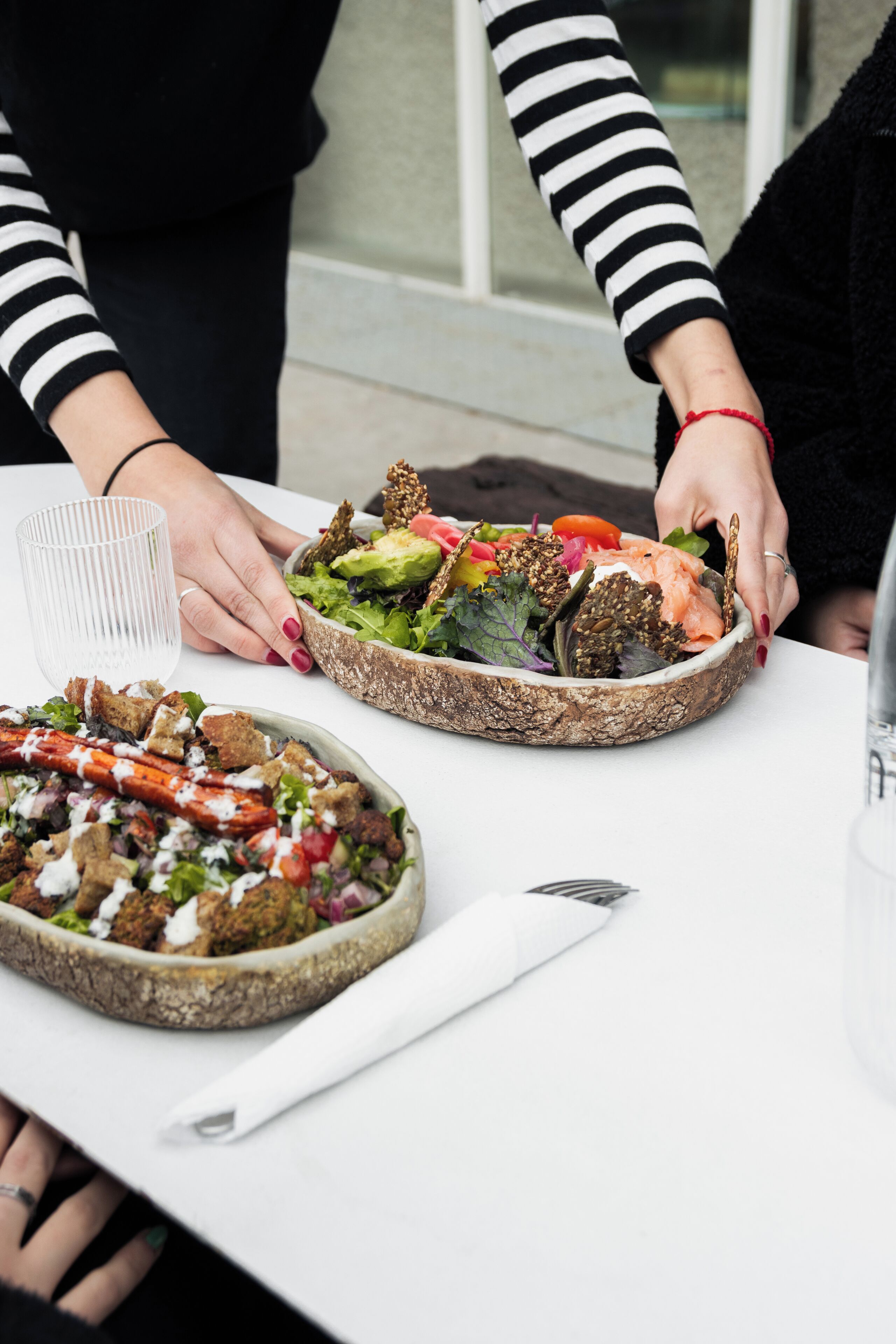 A table with two large bowls of food, a glass, and a napkin.