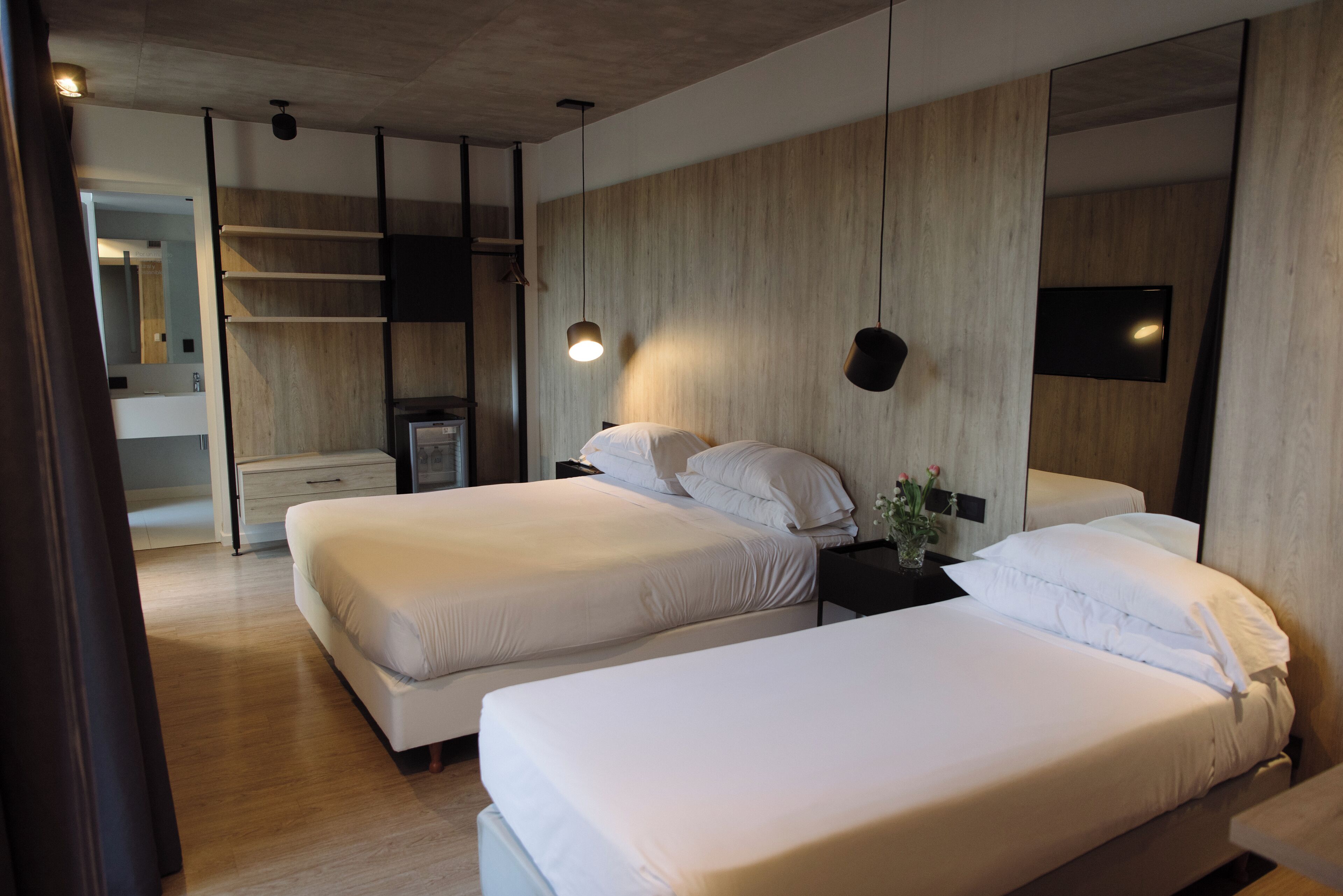 Una habitación de hotel moderna con dos camas, un revestimiento de madera, un televisor de pantalla plana y una mesita de noche con un florero.