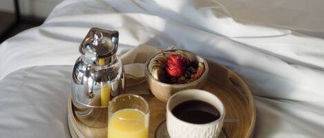 A breakfast tray with a coffee pot, a glass of orange juice, a bowl of fruit, and a cup of coffee on a bed.