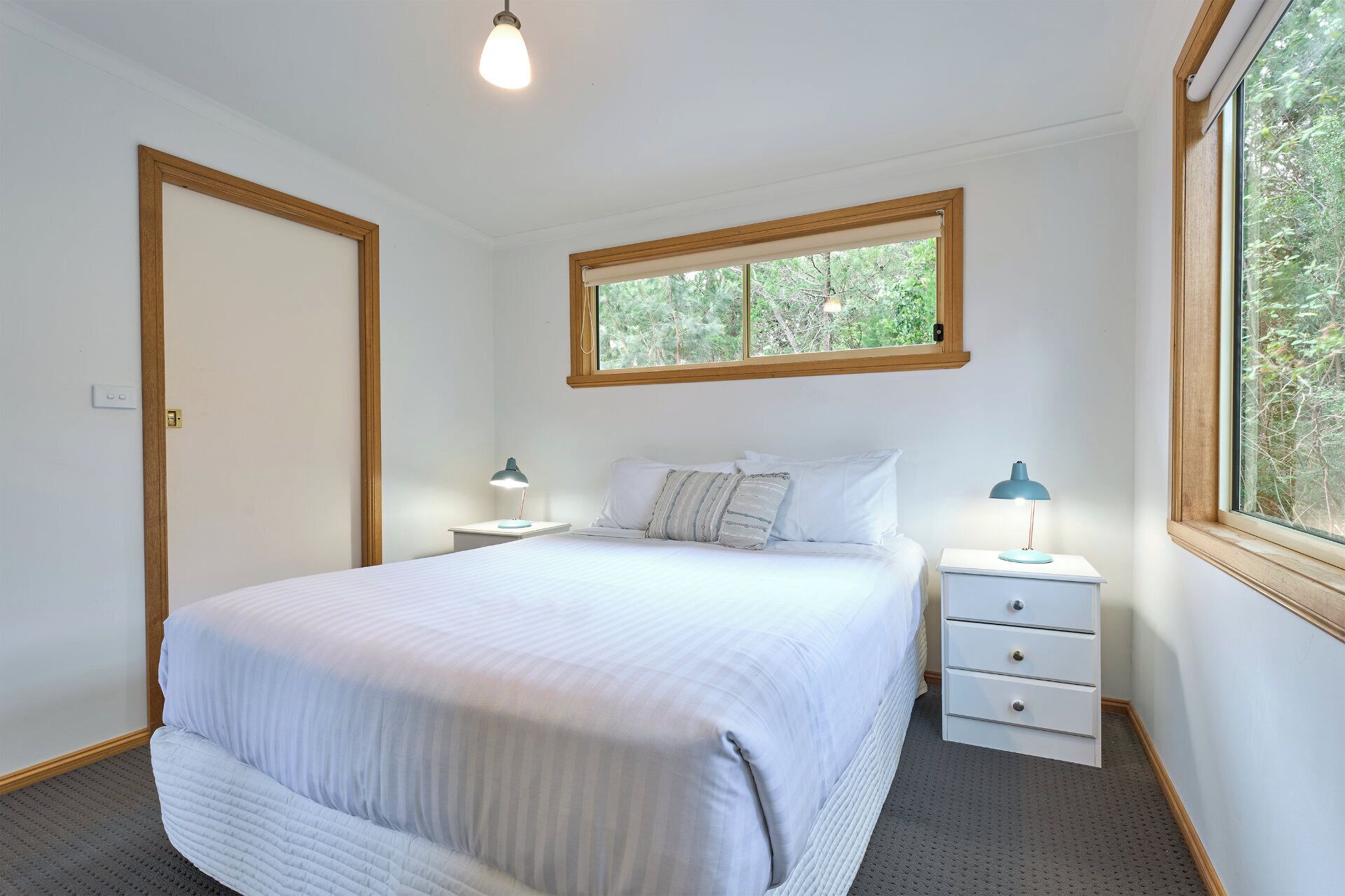 A bedroom with a bed, two bedside tables, a window, and a door.