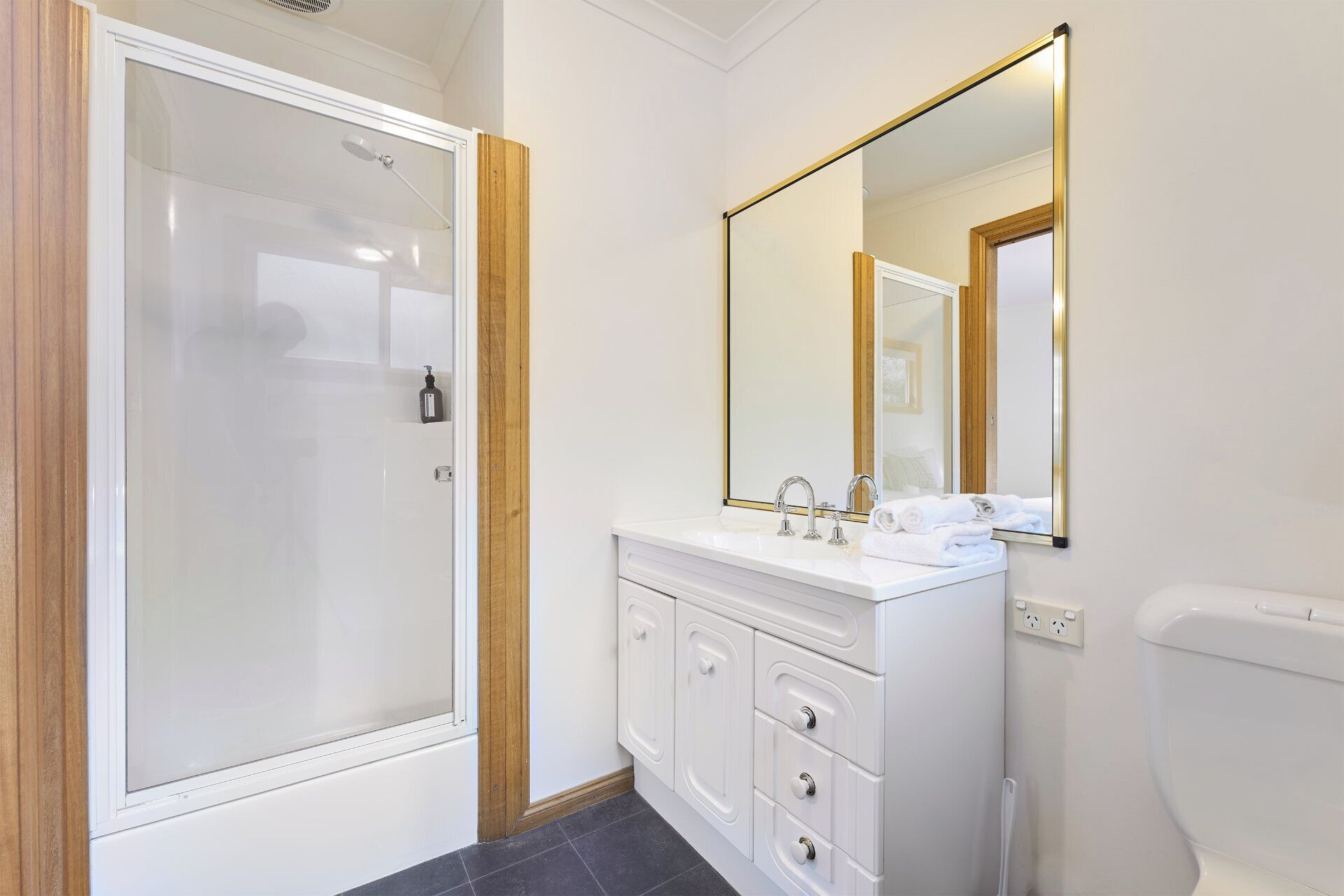 A bathroom with a glass shower enclosure, a white vanity with a mirror, and a toilet.