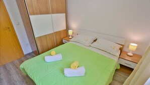 Una cama bien hecha con ropa de cama verde y dos toallas enrolladas, dos lámparas de noche y un armario de madera al fondo.