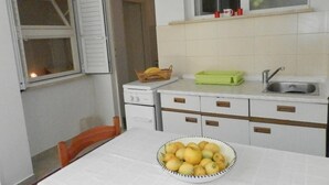 Une cuisine de taille réduite avec une table dressée pour le repas, un saladier rempli de fruits et une fenêtre dont les volets sont fermés.