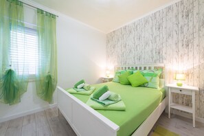 Quarto com cama, duas mesas de cabeceira, janela com cortinas leves e parede com padrão que imita madeira.