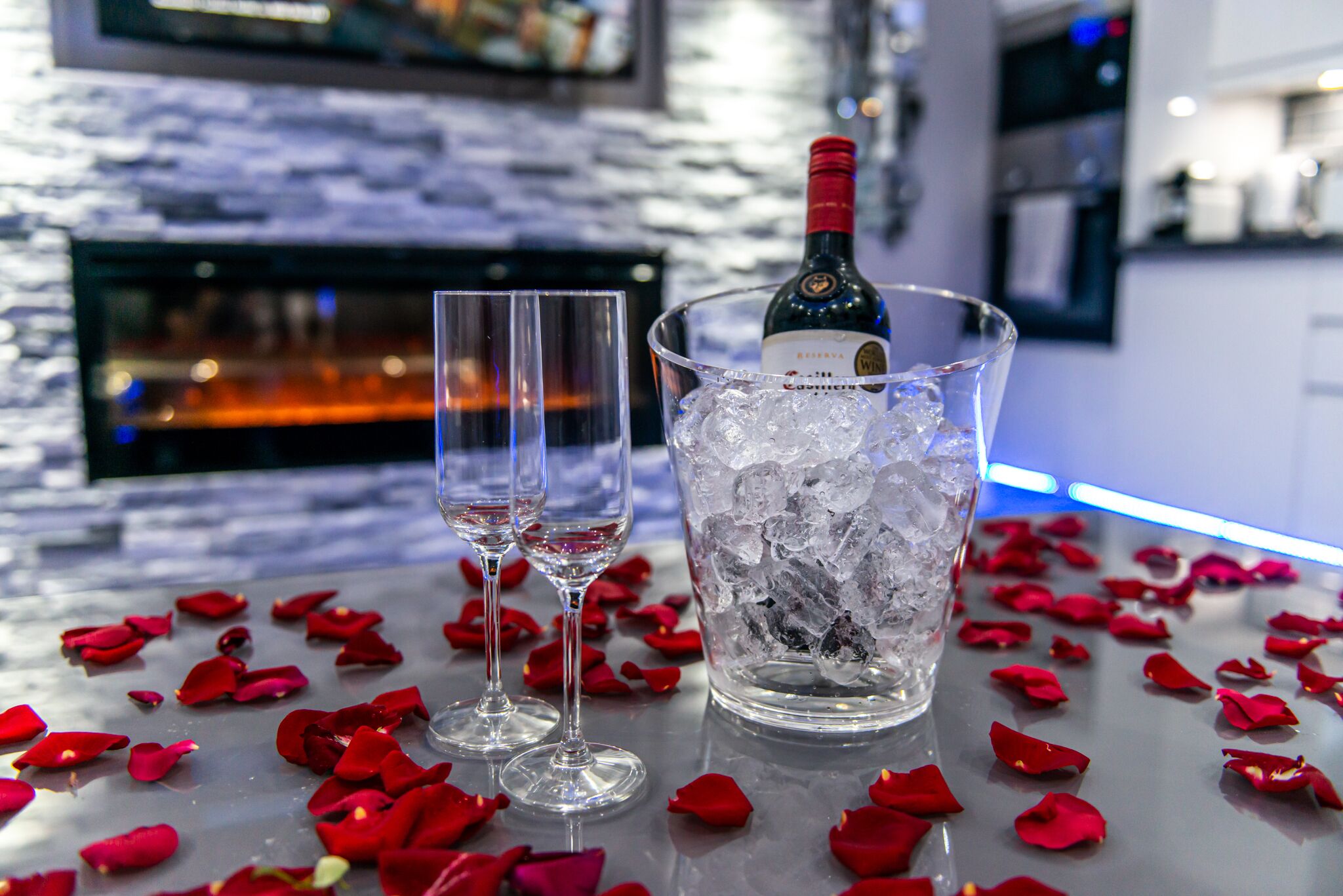 A bar setting with a bottle of wine, two glasses, and ice in a glass.