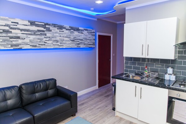 A modern kitchen with white cabinets, a black countertop, and a tiled backsplash. - Velmora Suites Bradford (Bradford)