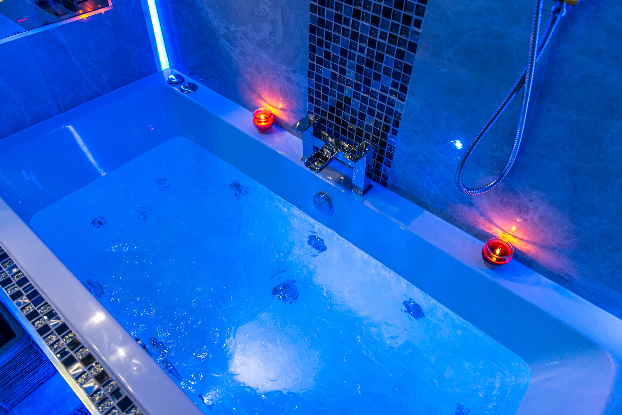 Une baignoire avec un éclairage bleu et deux bougies.